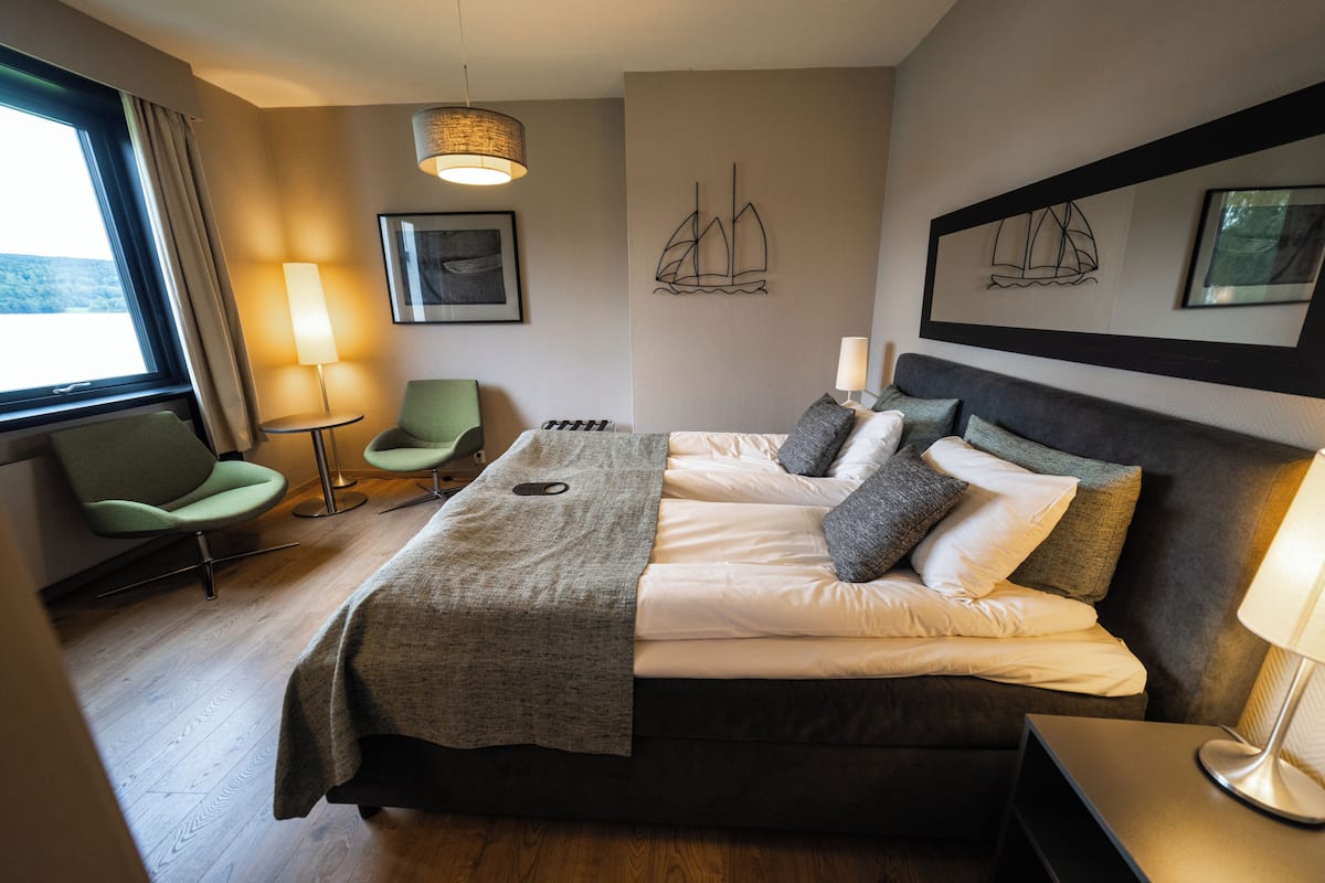 Una habitación de hotel con cama, una silla, una lámpara y obras de arte en las paredes.