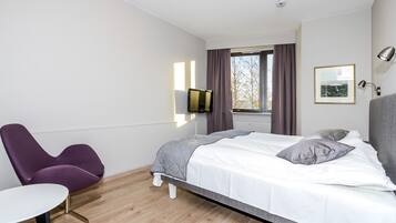 Una habitación de hotel moderna con cama, una silla, una mesita, televisor y ventana con cortinas.