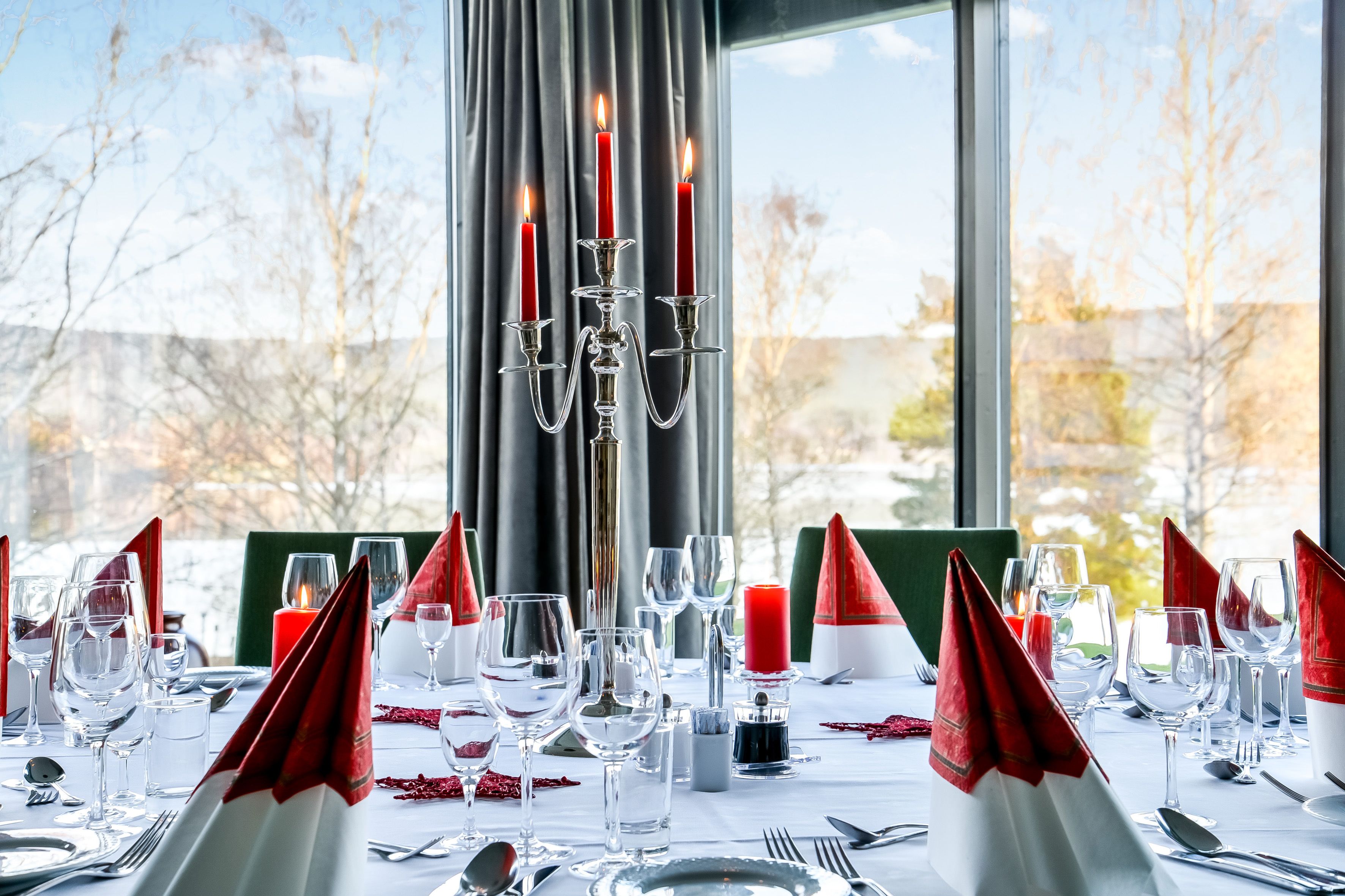 A formal dining table set with red napkins, clear glassware, and candles.
