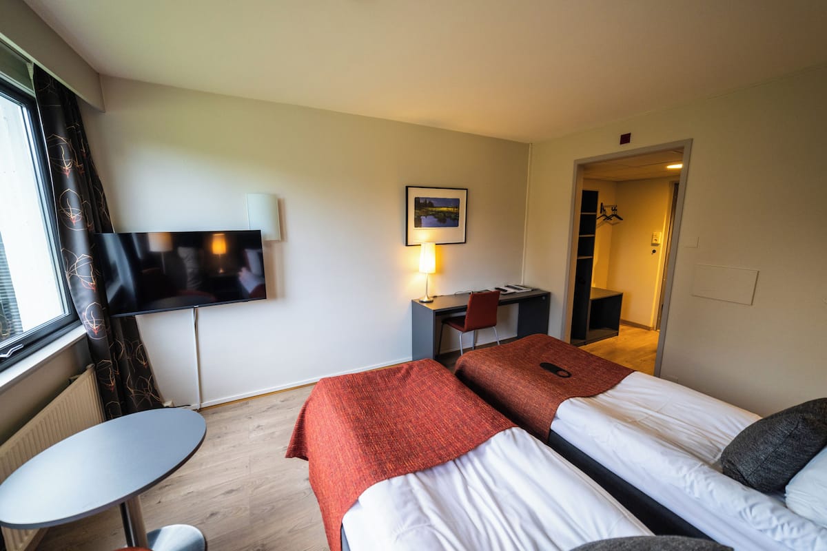 Una habitación de hotel con dos camas, un escritorio, una silla, un televisor y una mesita.