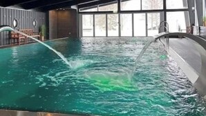 Una piscina interior con agua cristalina, un diseño moderno de techo y grandes ventanales que dejan entrar luz natural.