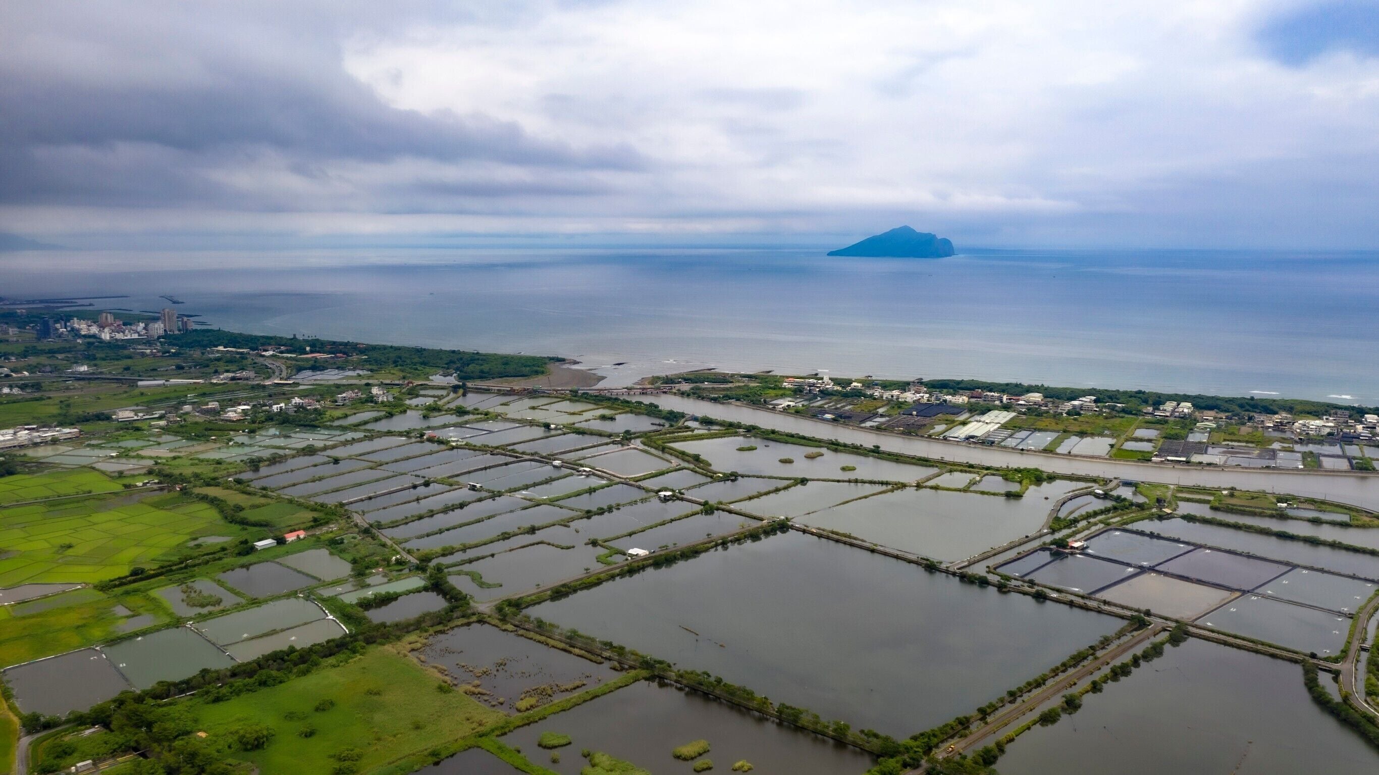 An aerial view of a coastal area with multiple water bodies and green fields.