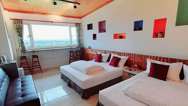 A hotel room with two beds, a sofa, a window with a view, and a wooden ceiling. - Waterbirds Family (Toucheng)