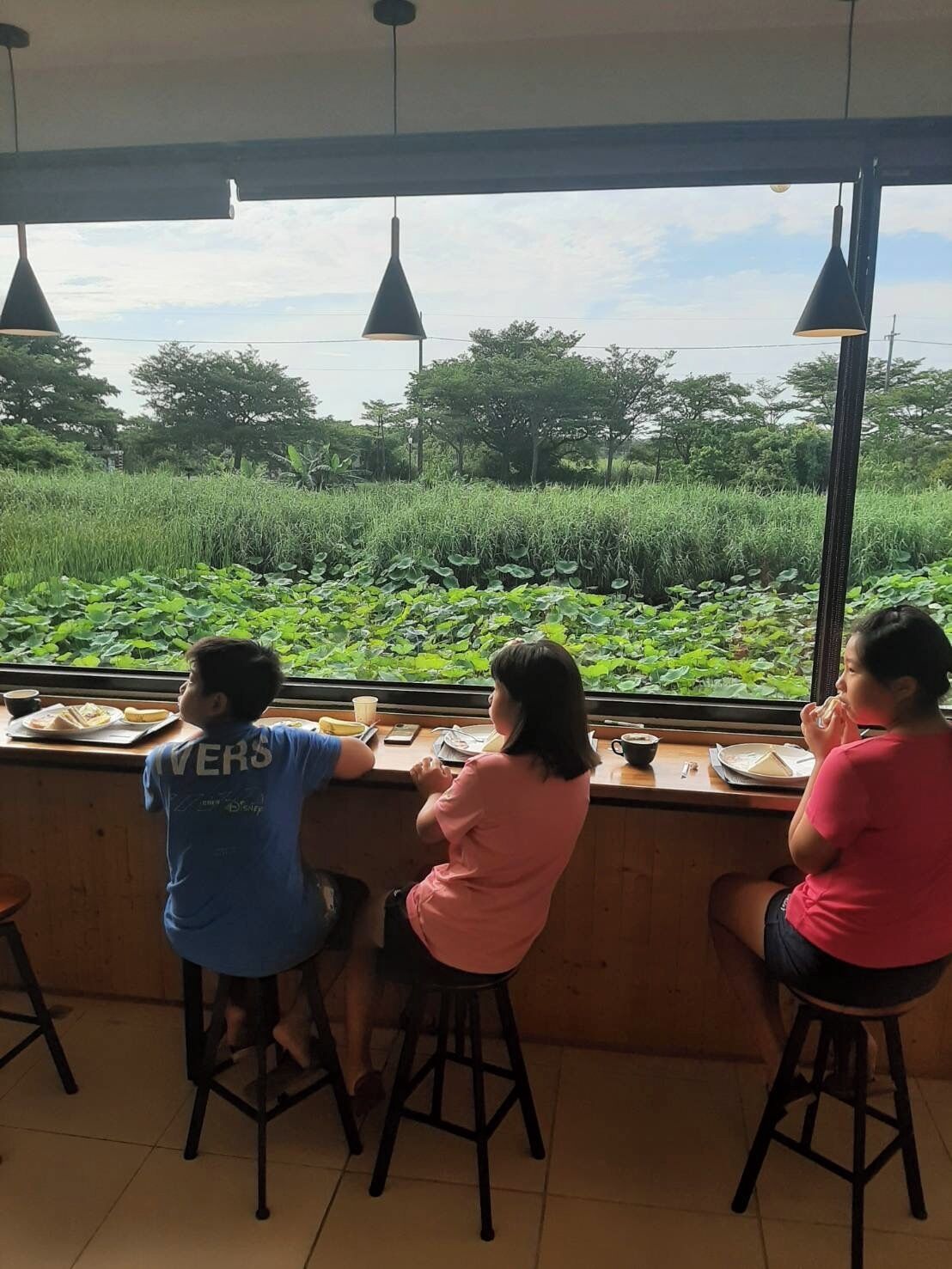 Three people seated at a counter with a view of a green field.