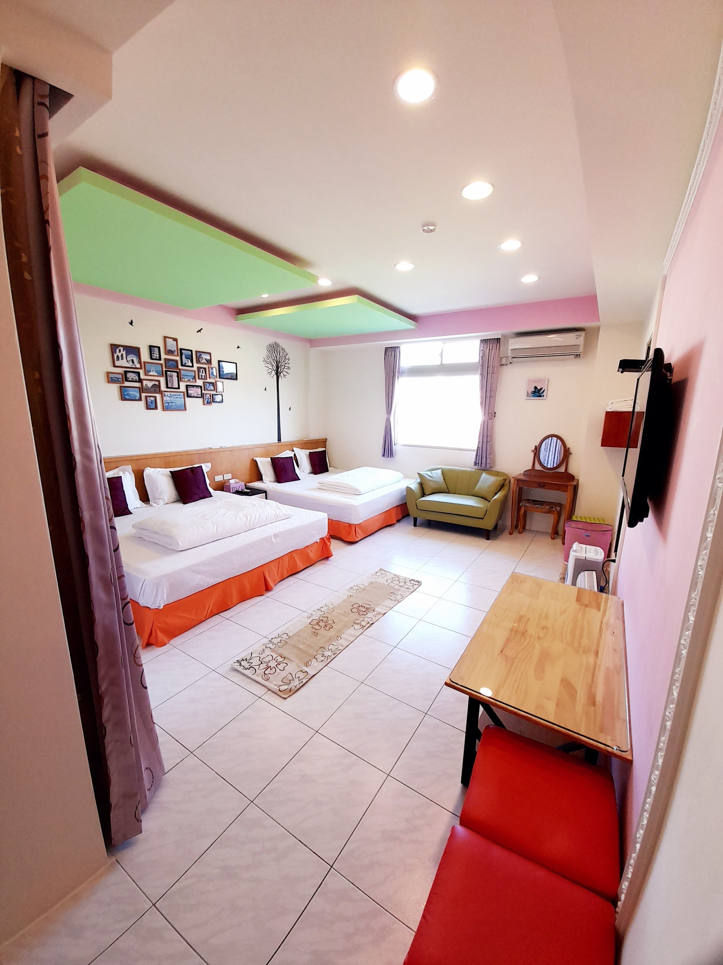 Habitación de hotel con dos camas, una mesita, una silla, un sofá, un espejo y un muro decorado con imágenes.