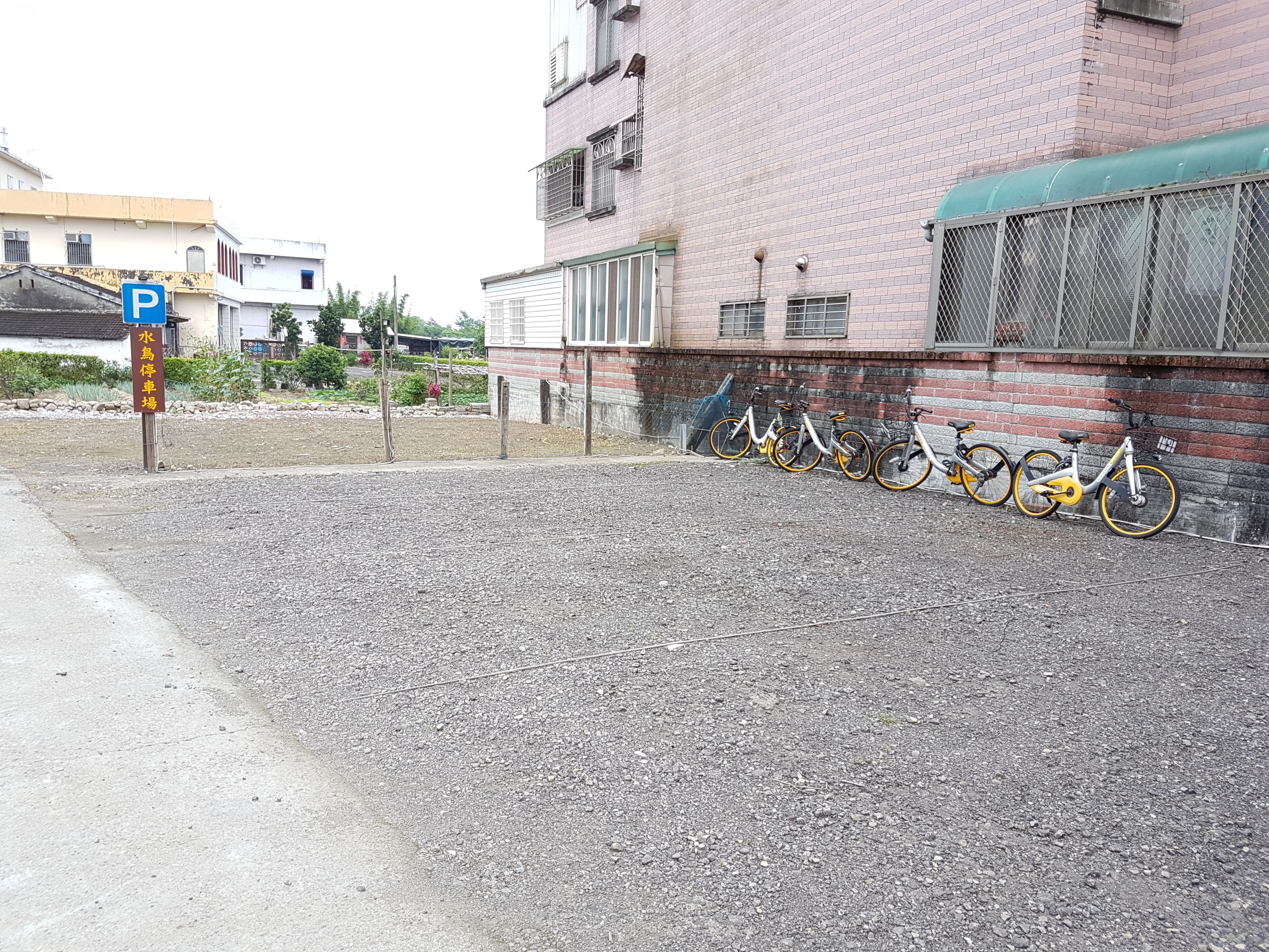 Un aparcamiento de grava con bicicletas estacionadas frente a un edificio de ladrillo.