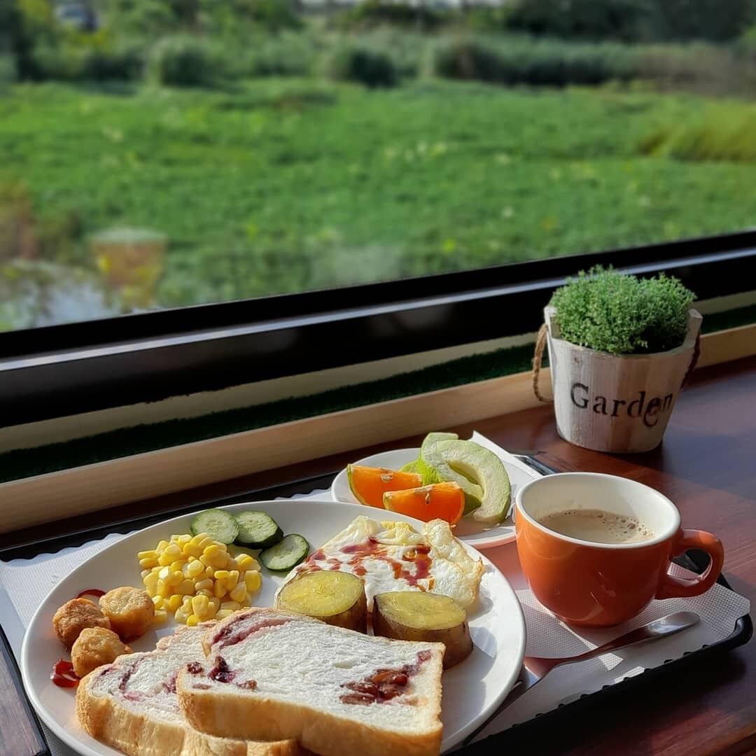 A meal tray with bread, vegetables, corn, and a cup of coffee on a table by a window with a view of greenery.