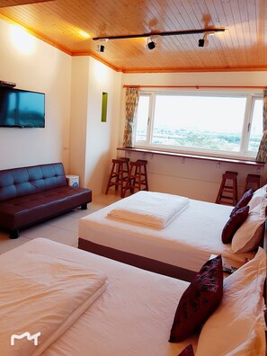 A hotel room with a wooden ceiling, a TV mounted on the wall, a bed with white linens, a red sofa, and a window with a view of the city. - Waterbirds Family (Toucheng)