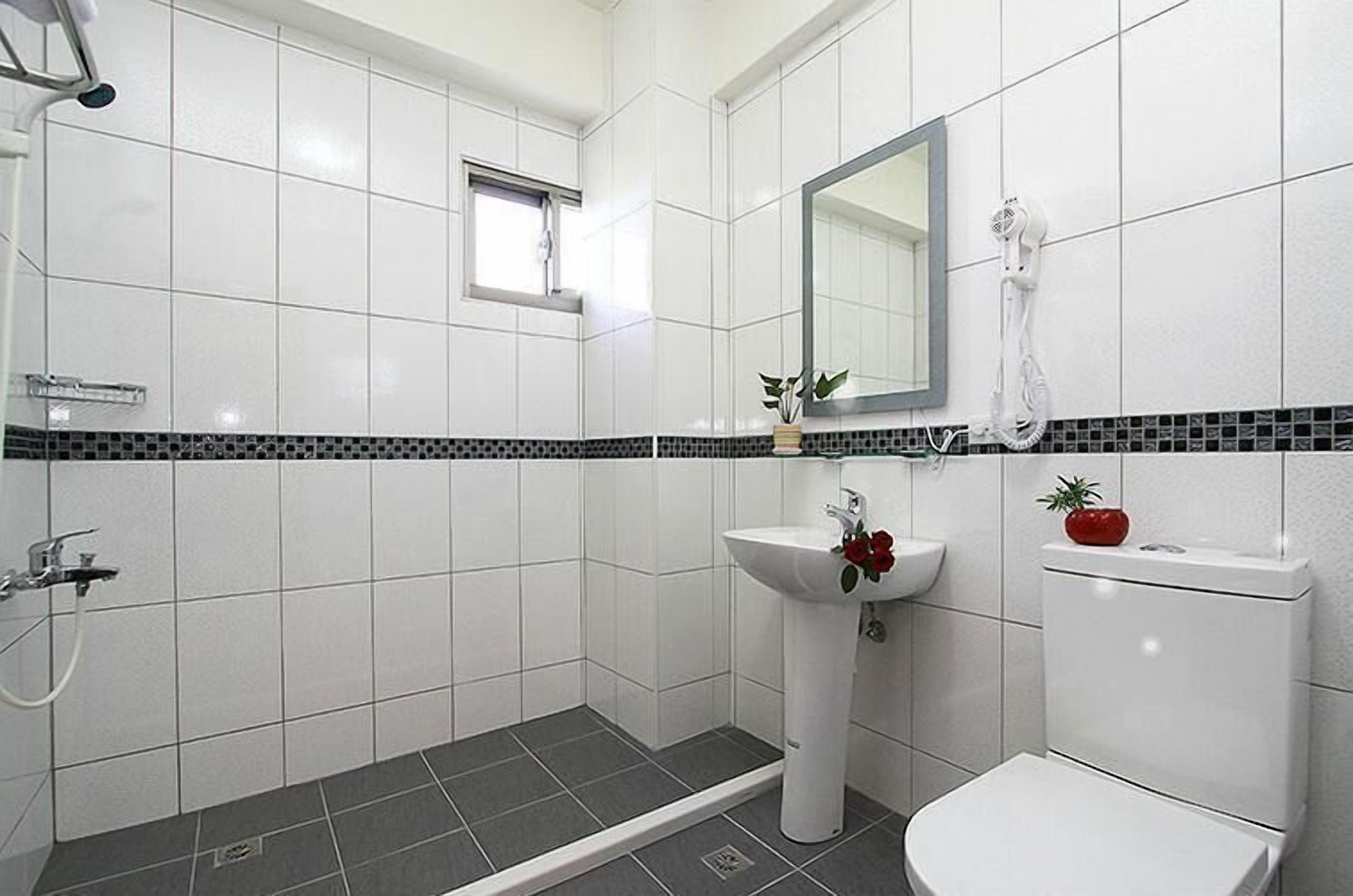 Kylpyhuone, jossa on valkoiset laatat, mustavalkoinen reunus, pesuallas, wc-istuin, suihku ja peili.