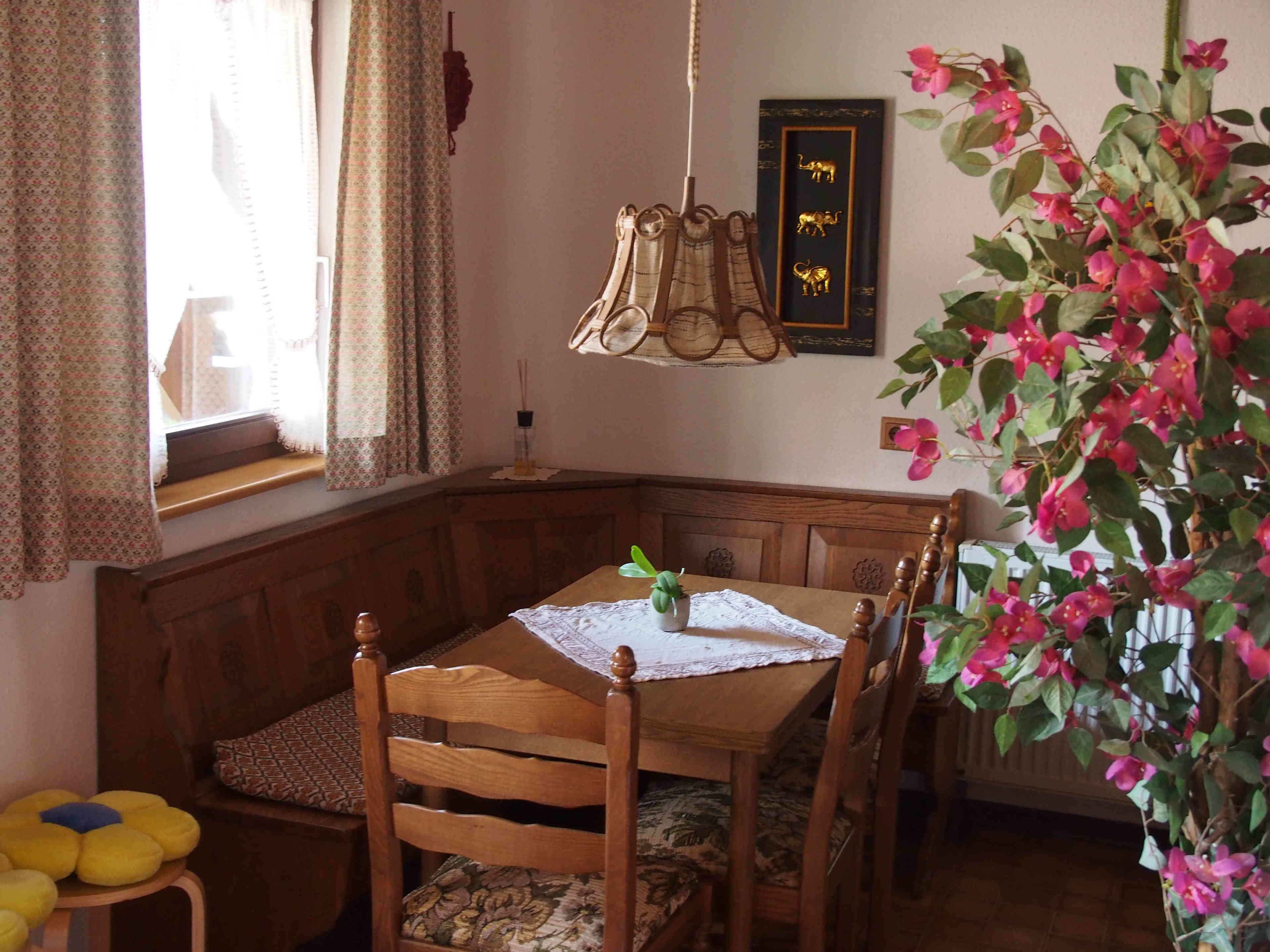 A corner dining area with a wooden bench, a table with a lace tablecloth, and a potted plant.