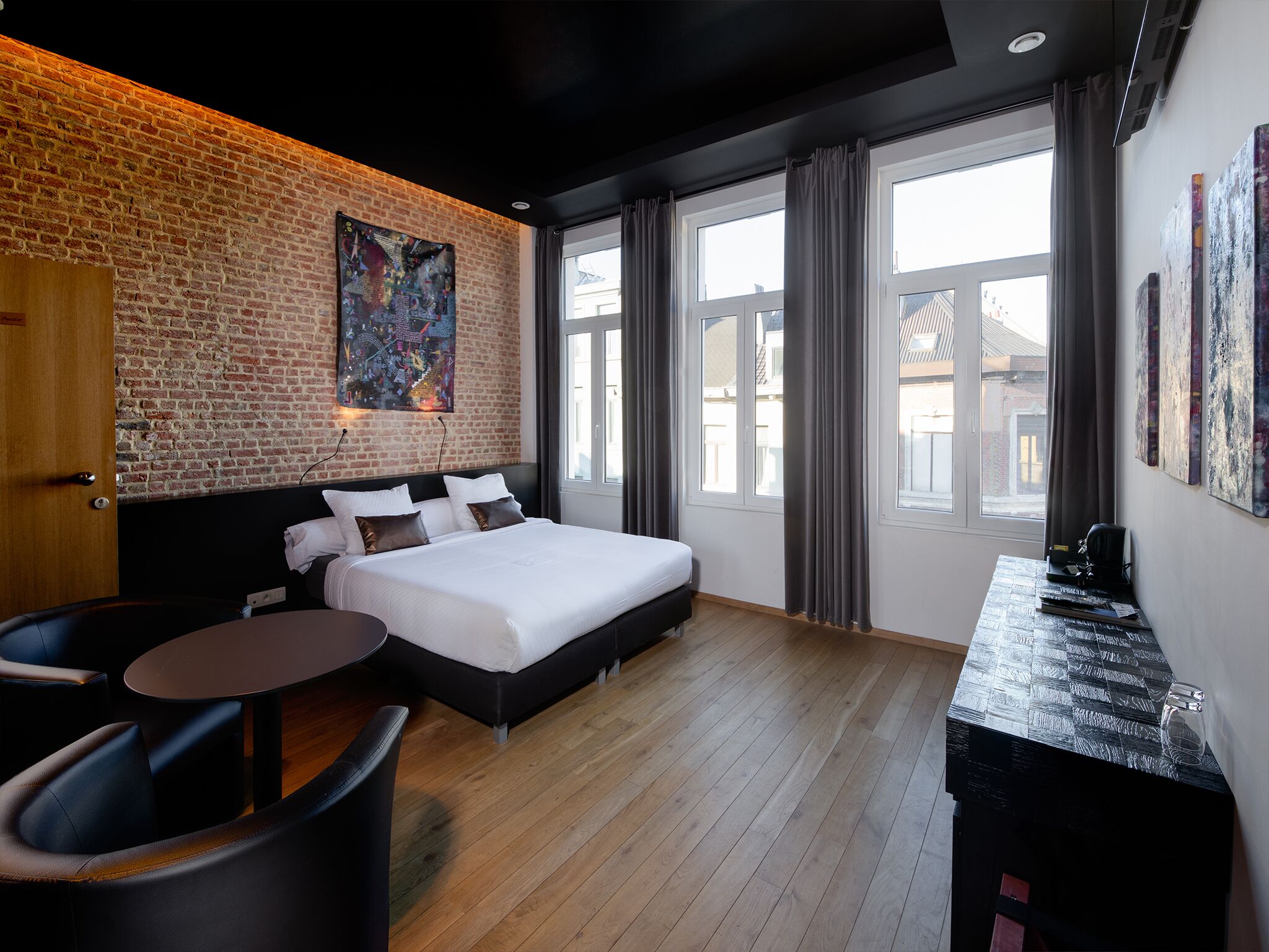 A modern hotel room with a brick wall, a large bed, a desk, and a view of the city.