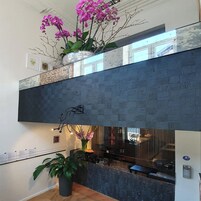 Ein modernes Interieur mit einer dunkel strukturierten Wand, einem Empfangstresen und Topfpflanzen.