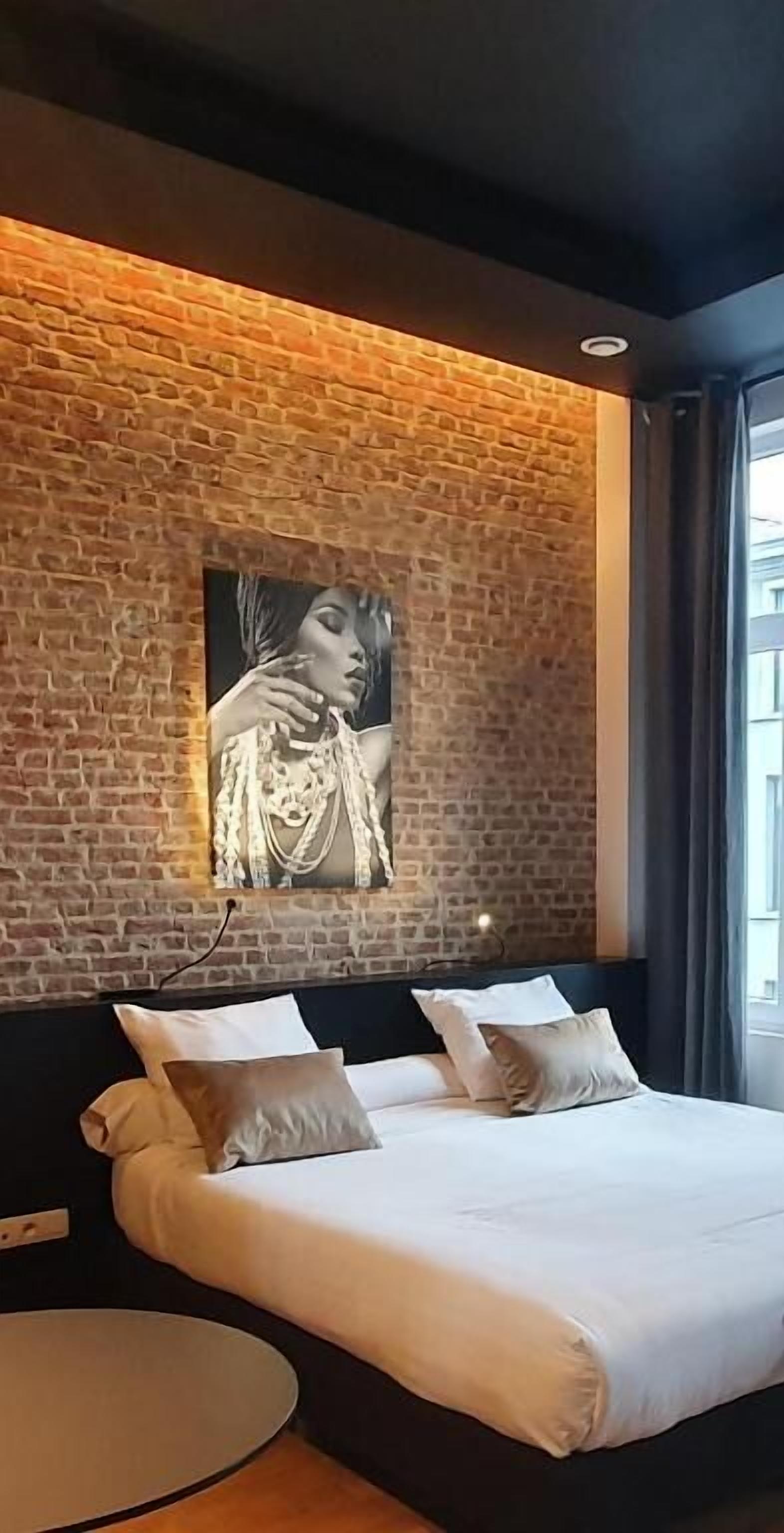 Un dormitorio moderno con pared de ladrillo, una cama grande con ropa blanca y un cuadro de una mujer.