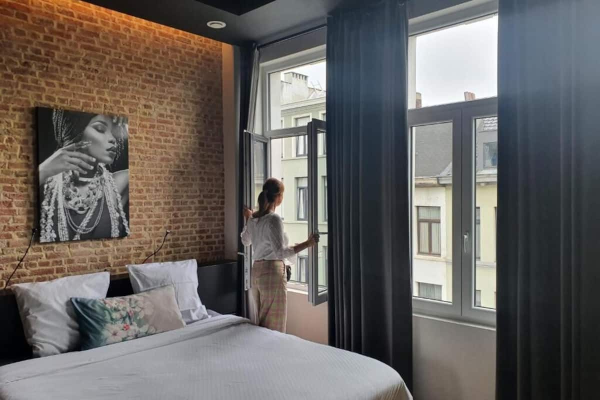 A bedroom with a large bed, a brick wall, a window, and a painting.