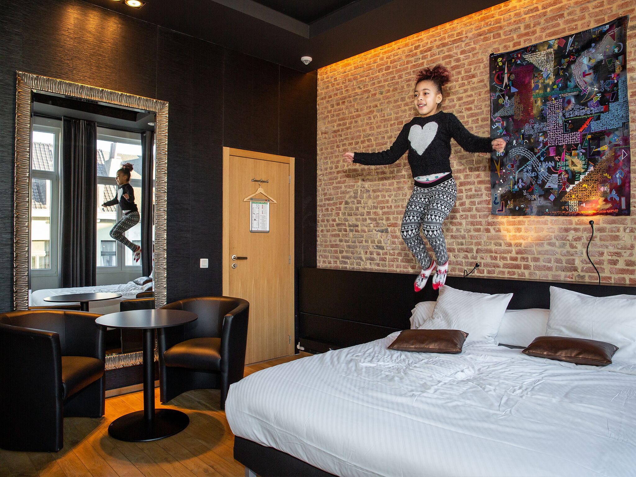 A room with a bed, a mirror, a door, and a colorful abstract painting on the wall.