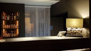Een bar met een plank vol drankflessen, een moderne lamp en een laptop op het aanrecht.
