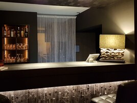 Eine Bar mit einer Flaschenregal voller Spirituosen, einer modernen Lampe und einem Laptop auf der Theke.