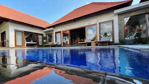 A modern poolside area with a clear pool, large windows, and a red-tiled roof. - Villa Tatiapi Ubud (Ubud)