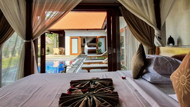 A hotel room with a bed, curtains, and a view of the pool and outdoor area. - Villa Tatiapi Ubud (Ubud)