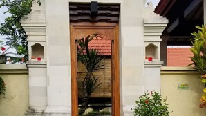 A building with a tiled roof, a central entrance with steps, and a small garden area with plants and a water feature. - Villa Tatiapi Ubud (Ubud)