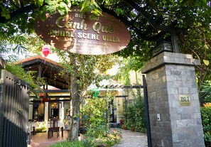 Uma vila rústica com uma placa, pilares de pedra e uma área de estar coberta ao ar livre.