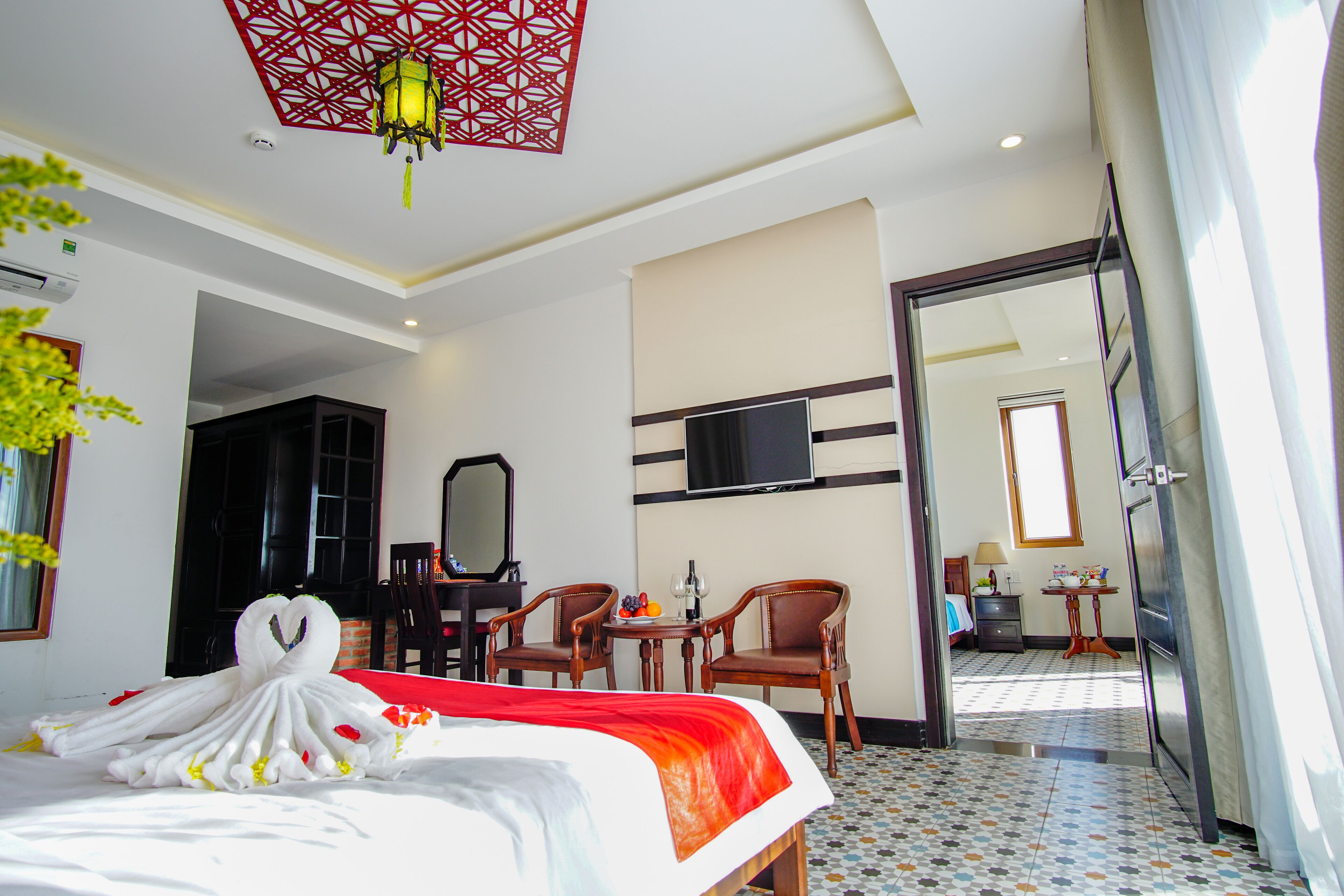 A hotel room with a bed, a TV, a desk with chairs, and a bathroom visible through an open door.