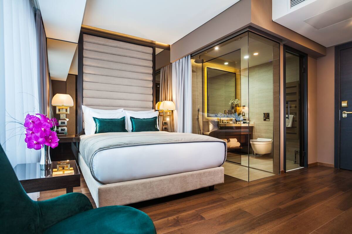 Une chambre d’hôtel moderne avec un grand lit, une salle de bain entièrement vitrée et un plancher en bois.