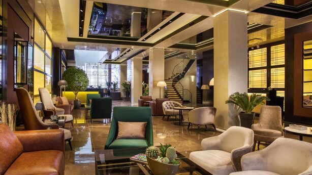 A spacious lobby with leather sofas, a green armchair, and a coffee table with a cactus centerpiece. A staircase is visible in the background. - SAINT TEN Hotel, Small Luxury Hotels (Belgrade)