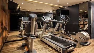 A modern gym with various cardio machines, a mirrored wall, and a wooden floor.