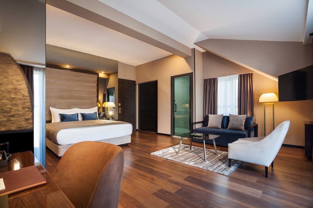 Une chambre d’hôtel moderne équipée d’un grand lit, d’un canapé, d’un fauteuil, d’un bureau et d’un téléviseur à écran plat.