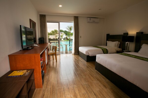 A hotel room with a TV, a desk, two beds, a chair, and a view of a pool and palm trees. - Gabi Resort & Spa (Cordova)