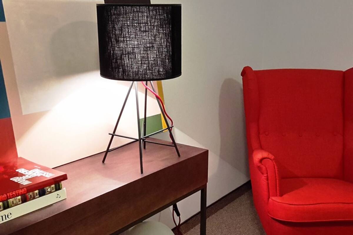A desk with a lamp, a red chair, and a stack of books.