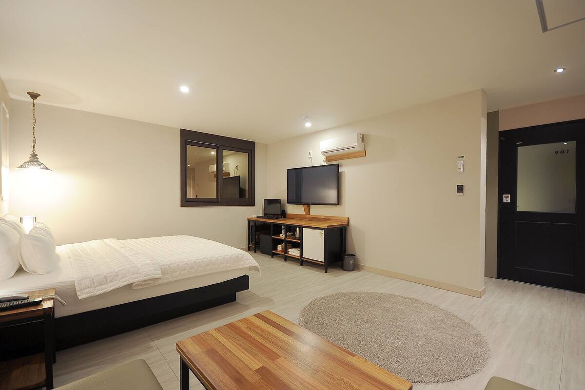 A bedroom with a bed, bedside table, desk, TV, and a door.
