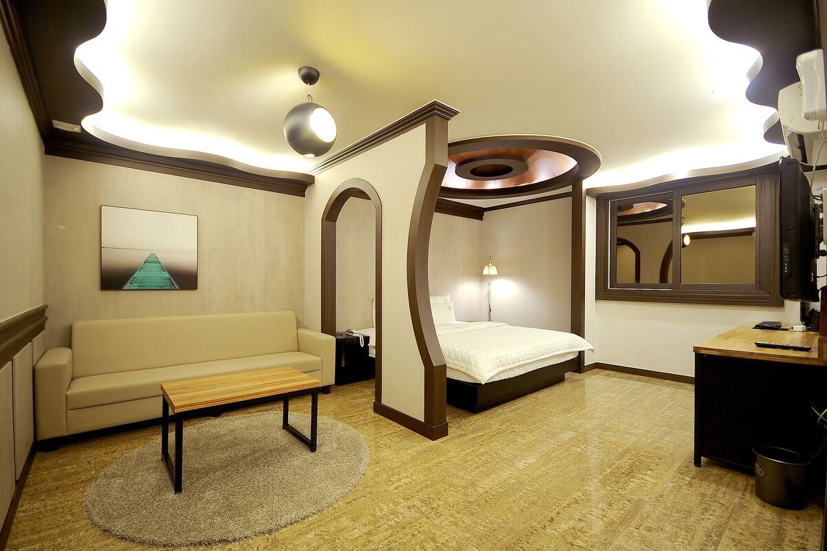A modern hotel room with a bed, a sofa, a desk, and a large mirror.