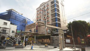 Un immeuble à plusieurs étages, de style architectural traditionnel, qui se distingue par une entrée imposante, un toit recouvert de tuiles et une enseigne.