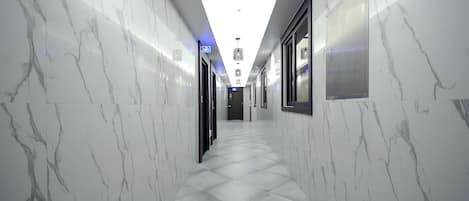 A modern hallway with marble walls and floor, leading to a door at the end.