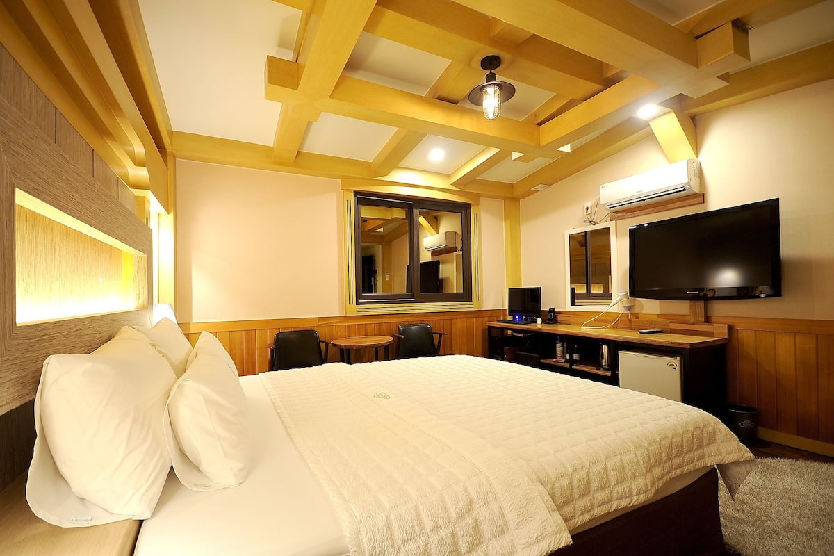 A hotel room with a bed, bedside table, TV, and a mirror.