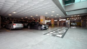 Un parking souterrain où sont garées plusieurs voitures, un plafond orné de motifs circulaires et un panneau avec du texte en coréen.