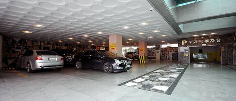 A parking garage with multiple cars parked, a ceiling with circular patterns, and a sign with Korean text.