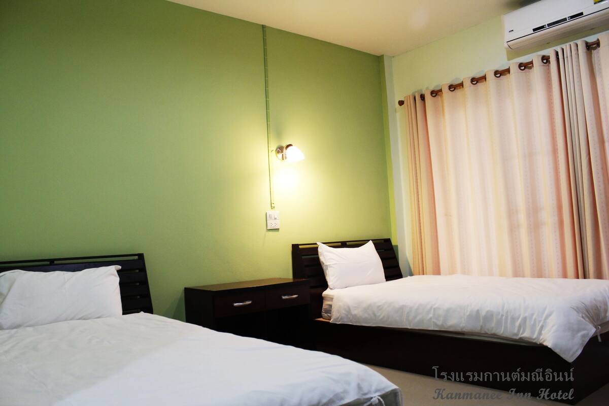 Habitación de hotel con dos camas, una mesita de noche, una lámpara de pared y una ventana con cortinas.
