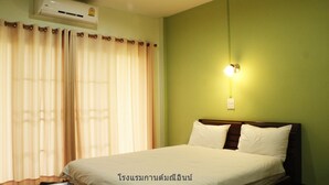 A hotel room with a bed, curtains, an air conditioner, and a wall-mounted light. - Kanmanee Inn (Chiang Rai)