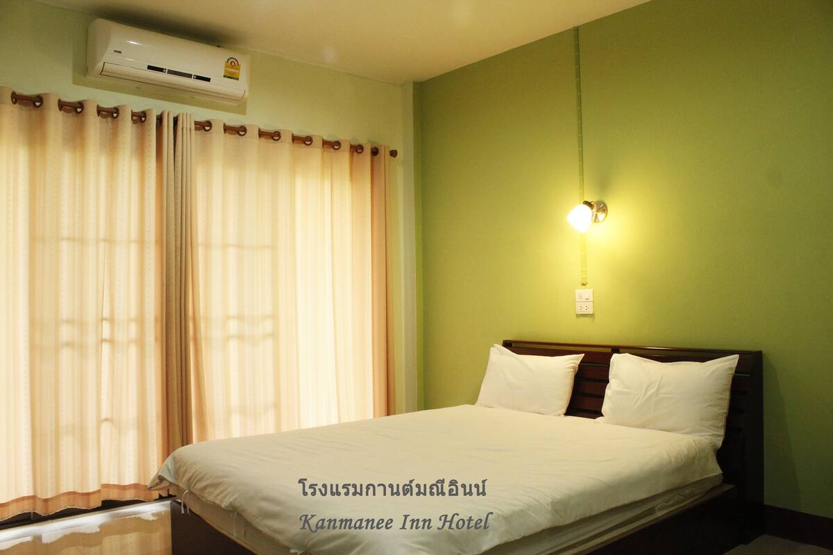 Una habitación de hotel con cama, cortinas, aire acondicionado y una lámpara fijada a la pared.