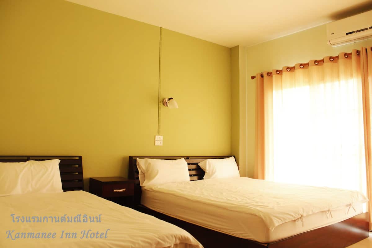 Habitación de hotel con dos camas, una mesita de noche, una lámpara de pared y una ventana con cortinas.