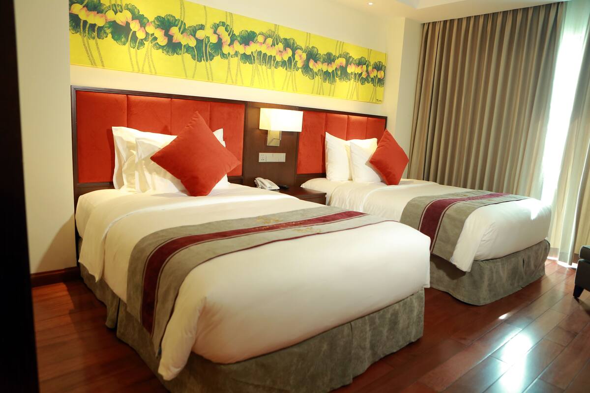 Quarto de hotel com duas camas, um quadro grande na parede e uma janela com cortinas.