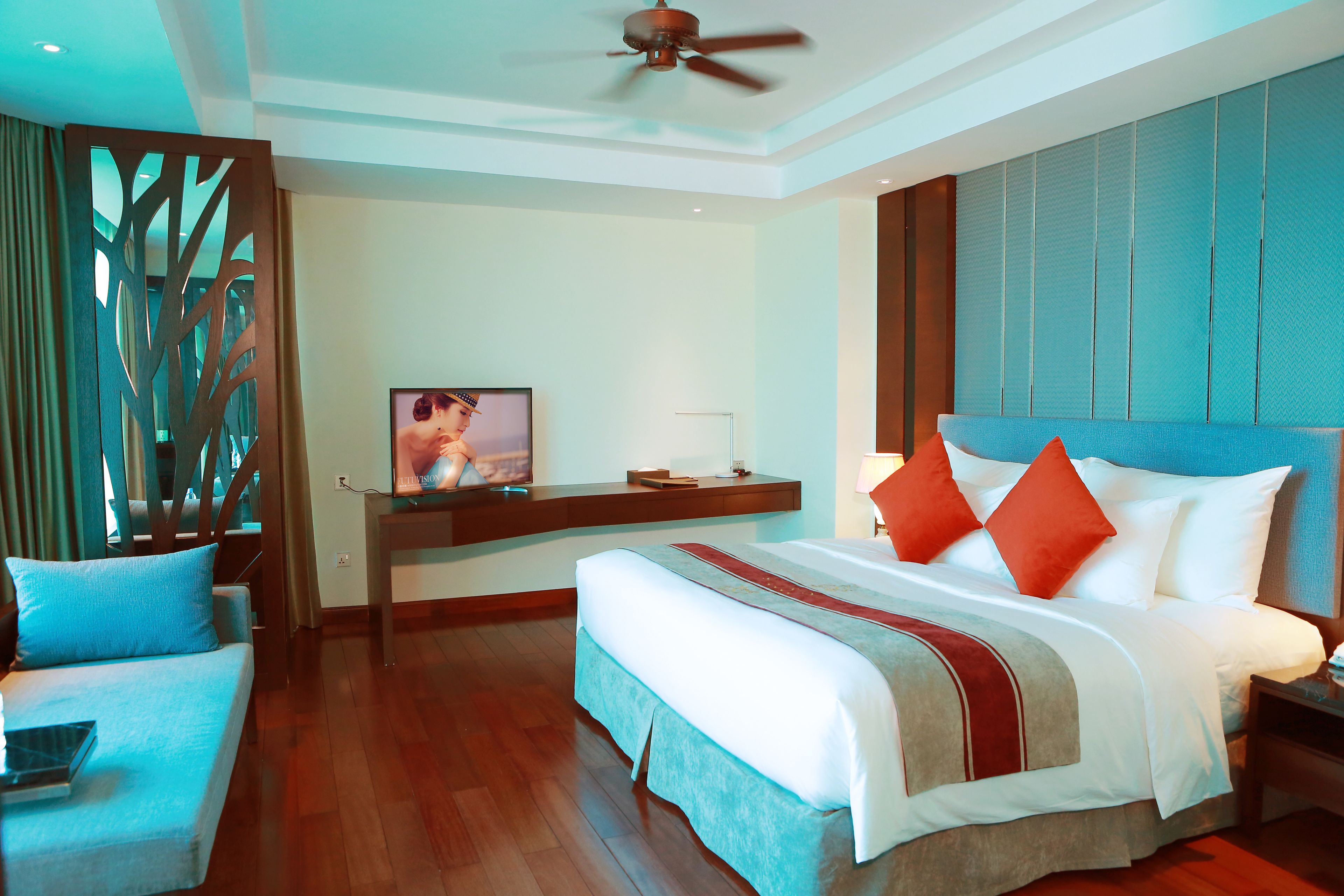 A hotel room with a large bed, a desk with a television, and a ceiling fan.
