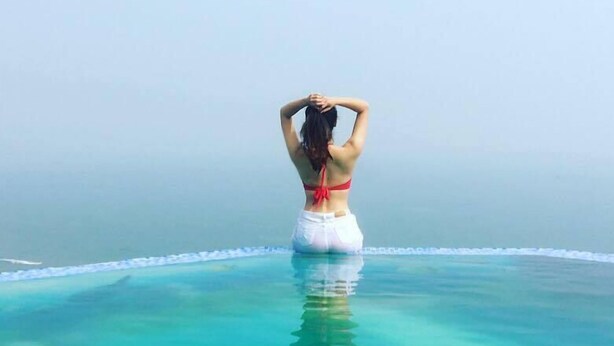 Una persona de pie al borde de una piscina infinita azul y cristalina, con vista al océano.