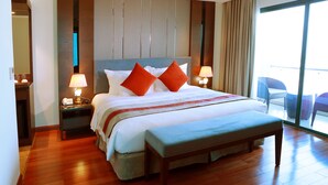 Habitación de hotel con una cama grande, dos mesitas de noche con lámparas, un banco y vistas al balcón exterior.