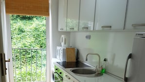 A kitchen with white cabinets, a sink, a coffee maker, and a view of greenery outside. - Taban Hostel Zagreb - hostel (Zagreb)