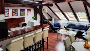 A loft-style room with a wooden ceiling, skylights, a bar area with chairs, a sofa, and a dining table. - Taban Hostel Zagreb - hostel (Zagreb)