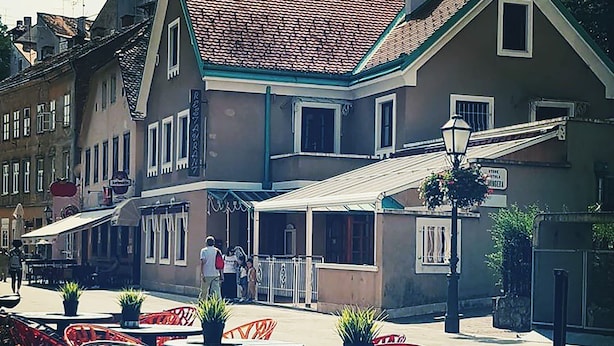 Outdoor seating with tables and chairs, a building with a tiled roof, and a street in the background. - Taban Hostel Zagreb - hostel (Zagreb)
